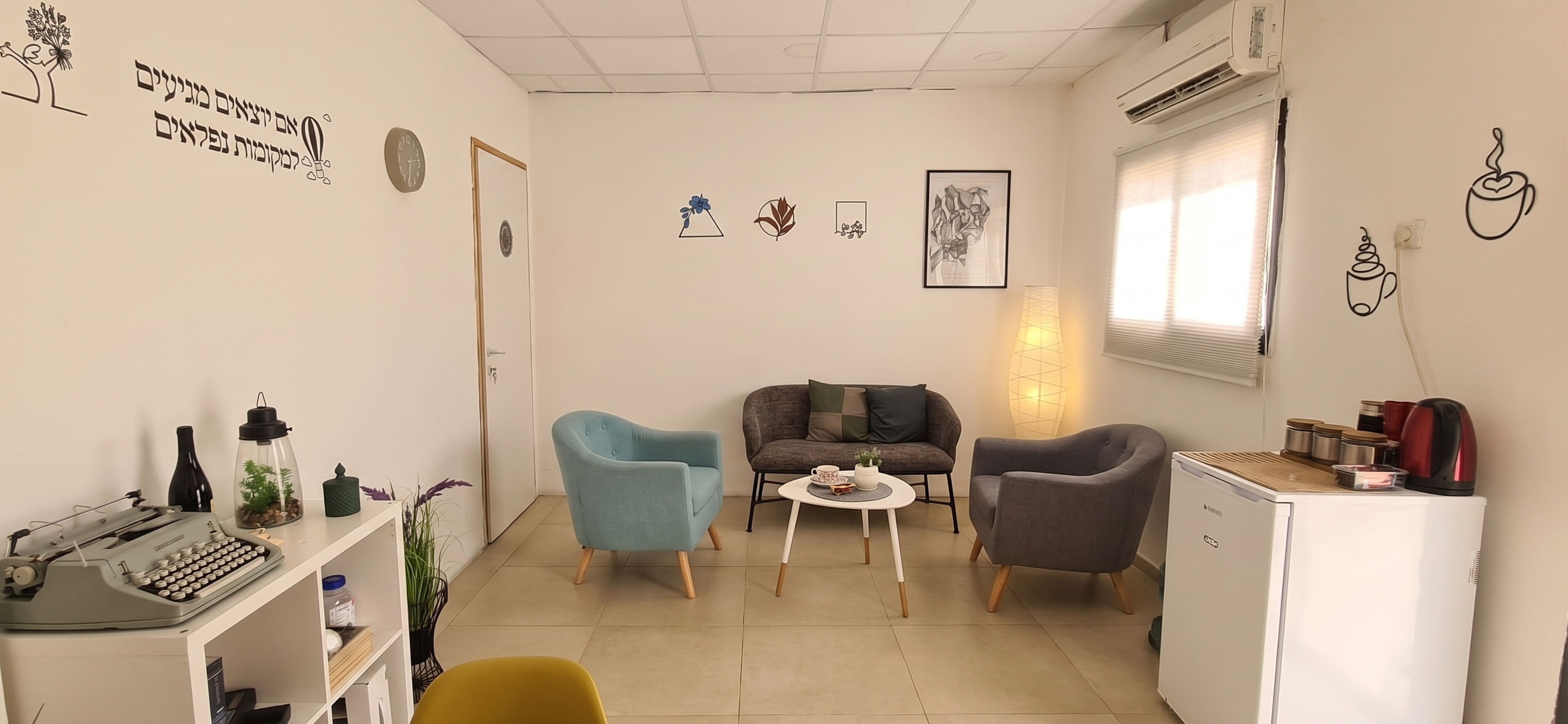 חדר המתנה מואר ומעוצב בגוונים רגועים עם כורסאות, ספה, שולחן קפה ופריטי נוי שונים.